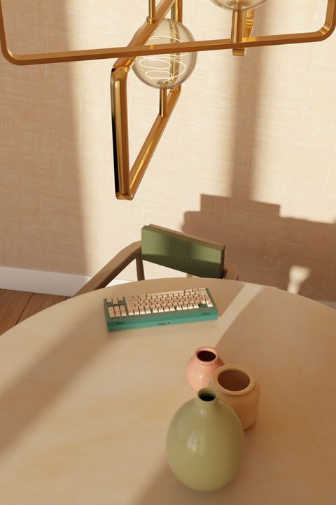 The keyboard on a table under a brass pendant light, with green and pink vases in the foreground