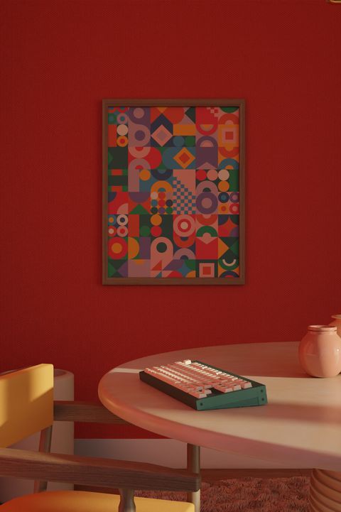 The keyboard on a pale table against a deep red wall, the colourful Abstract pattern framed above it