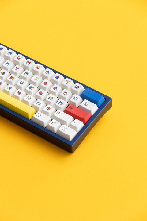 Navy mechanical keyboard with Mondrian-style geometric keycaps against a yellow background