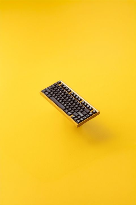 Yellow mechanical keyboard with black keycaps floating against a yellow background