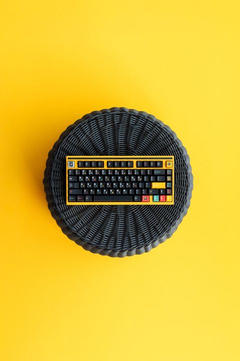 GMK Tribal keyboard on a black woven rattan mat against a yellow background