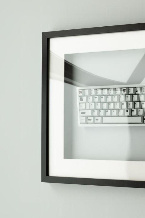White mechanical keyboard displayed like art in a black picture frame mounted on a wall