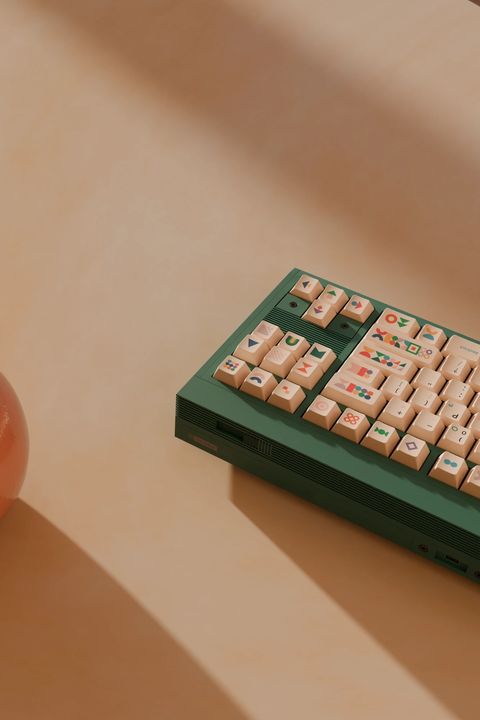 A green keyboard on a peach tabletop, seen from above at an angle, its shape novelties lit by soft diagonal shadows beside an orange sphere